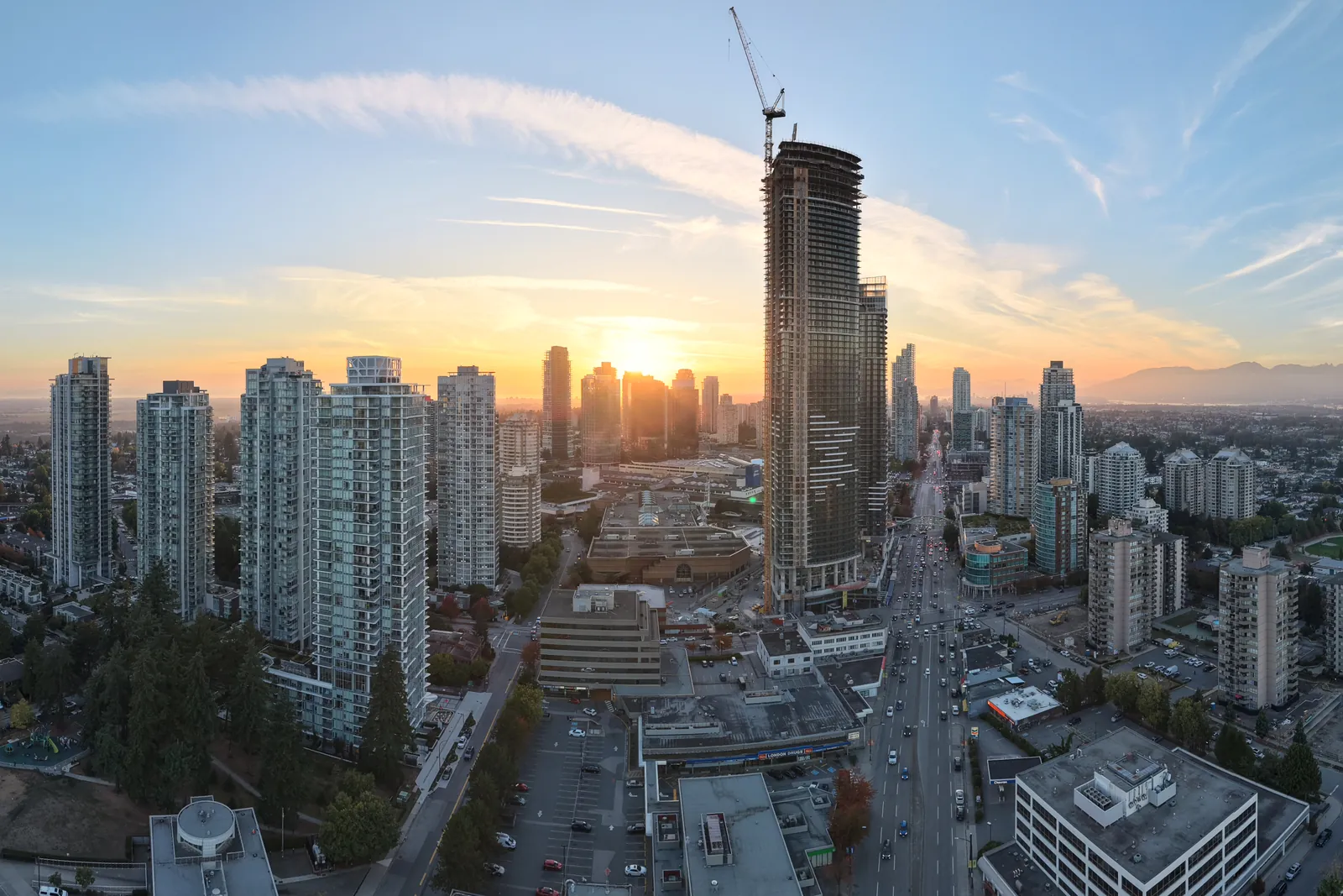 Aerial view of the Metrotown skyline at sunset, with the sun setting between the towers and a tall tower under construction topped by a crane