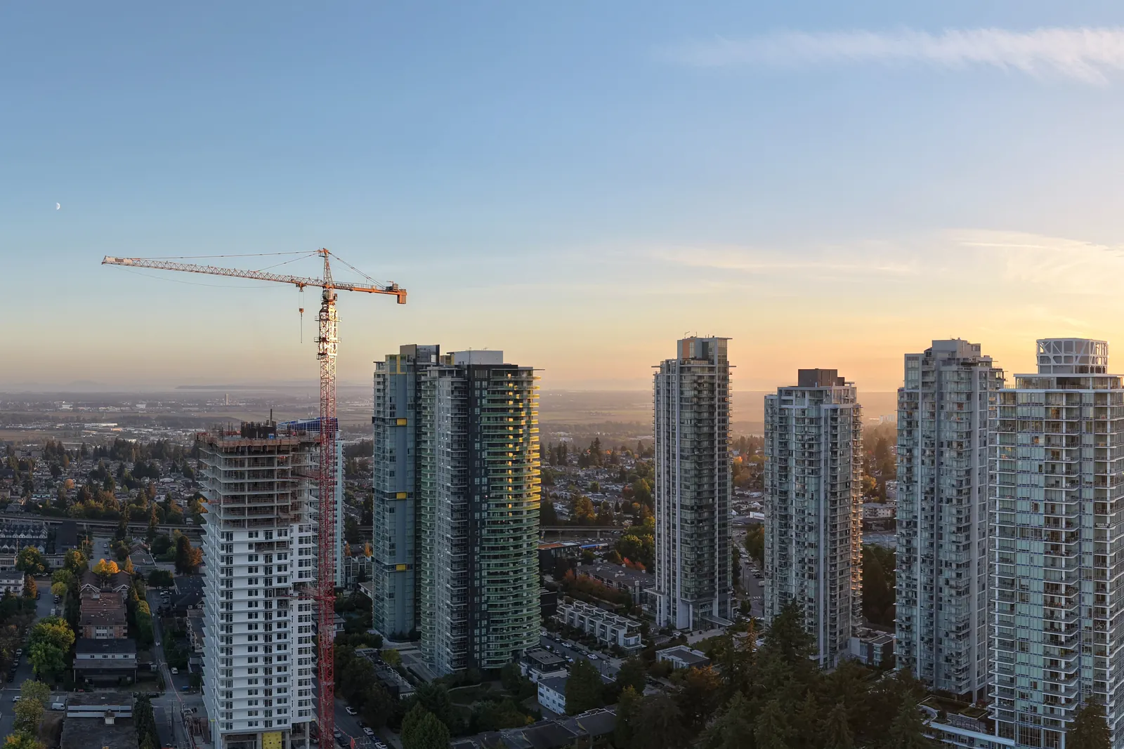 Residential towers in Burnaby's Metrotown area at sunset, with a red tower crane beside a tower under construction