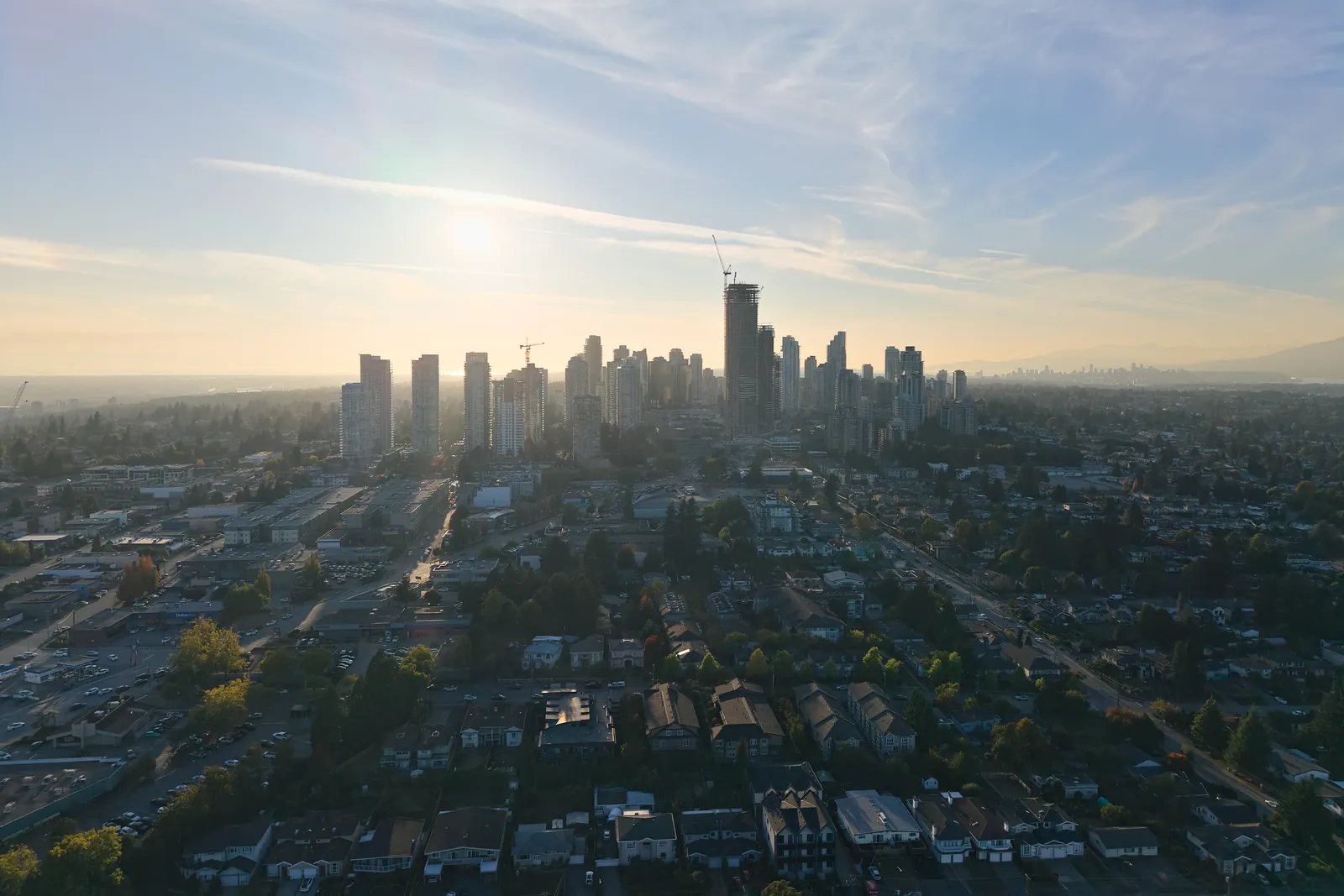 Metrotown towers against a hazy golden-hour sky, with low-rise commercial buildings and homes in front