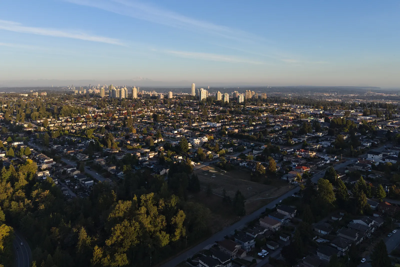 South Burnaby homes and tree-lined streets in evening light, with distant towers on the horizon